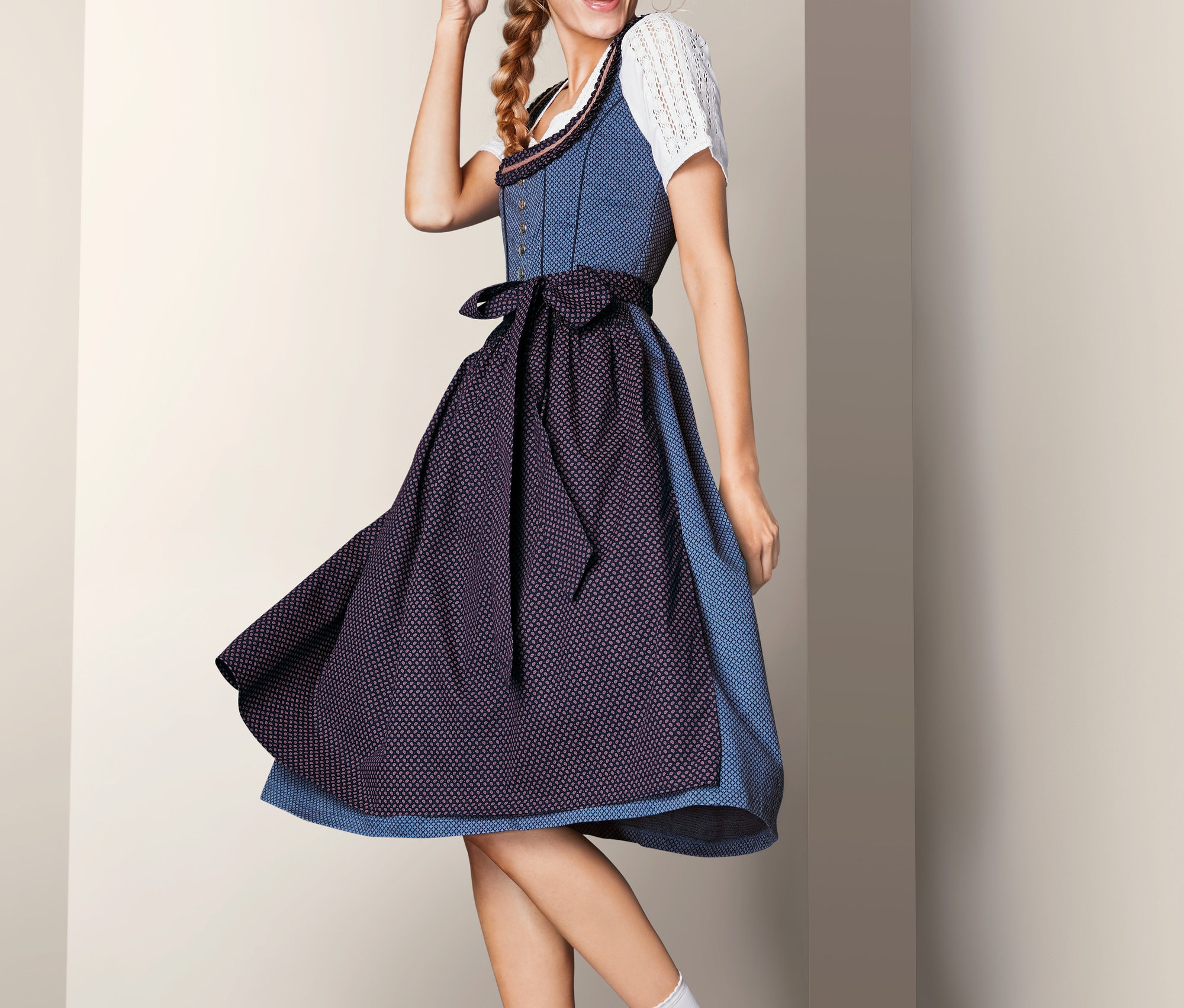 Frau lächelt und posiert in einem blauen Stretch-Dirndl, einer weißen Bluse und Turnschuhen.