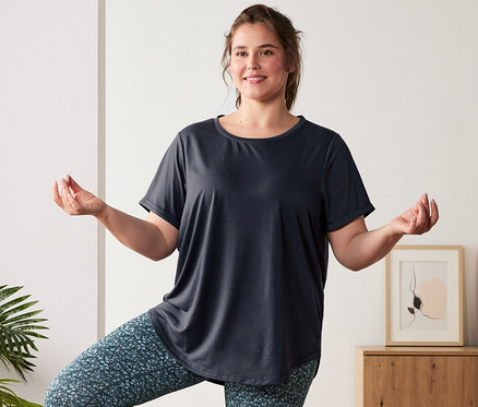 Eine Frau in Longshirt, grau-blau, und blauer Wende-Sporttight steht auf einer blauen Yogamatte. Sie trägt 3 Paar Socken, blau.