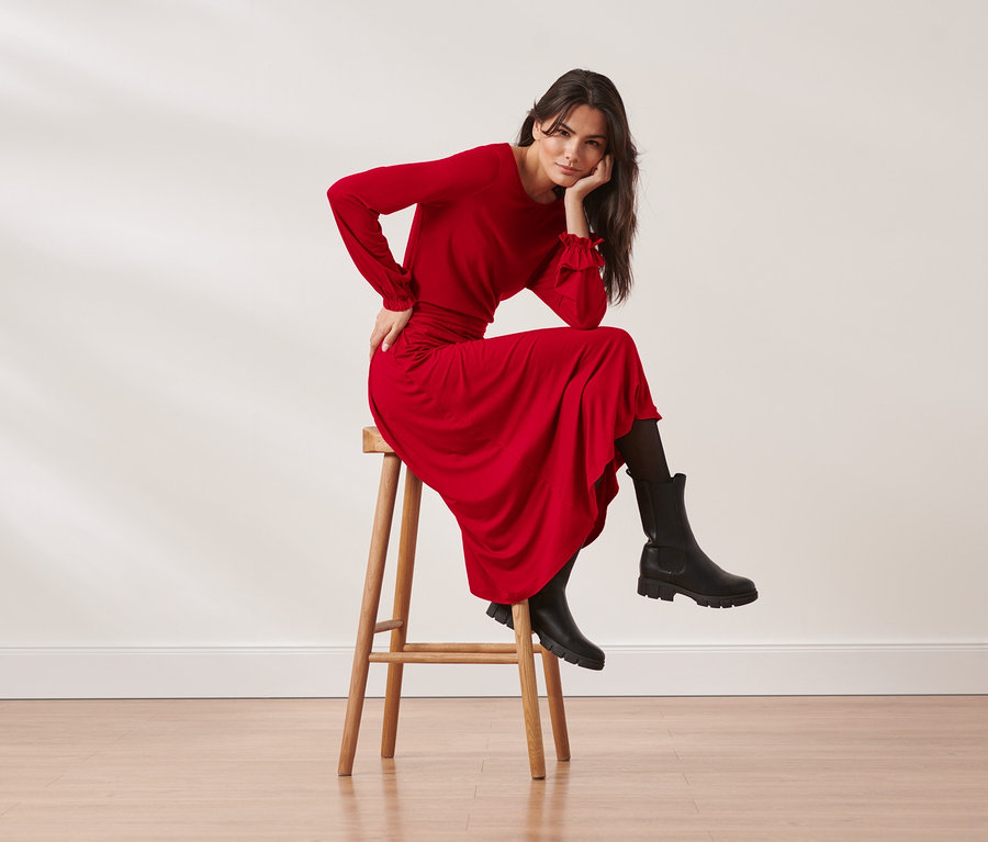 Frau sitzt auf einem Hocker und trägt ein rotes Jerseykleid in Midilänge.