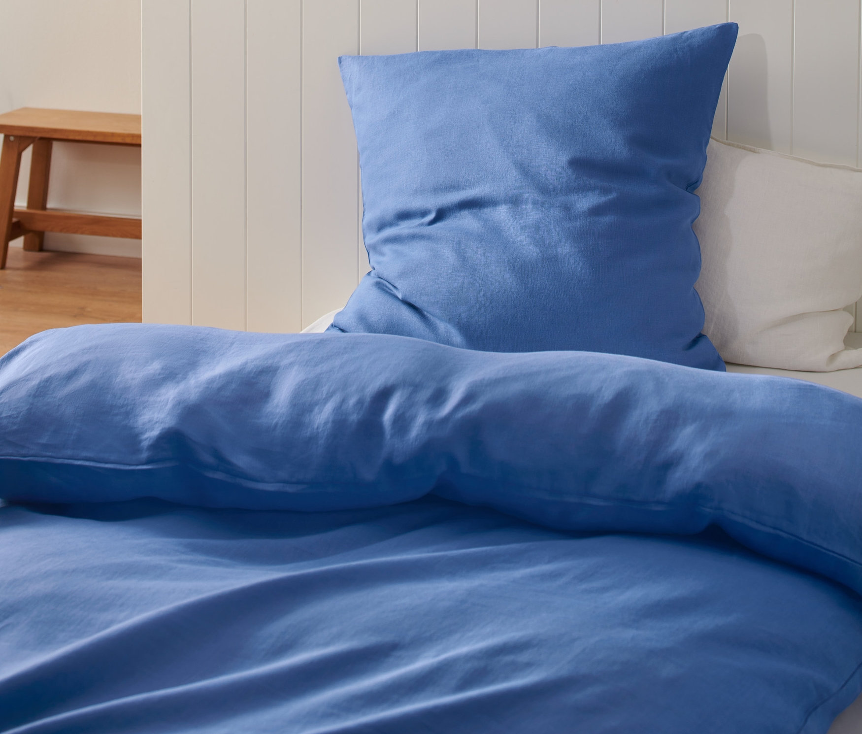 Blaue Leinenbettwäsche auf einem Bett mit weißem Kopfteil.