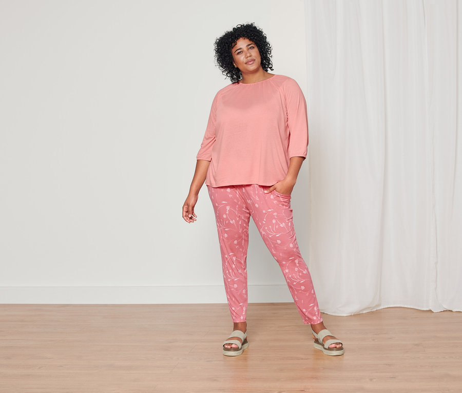 Eine Frau posiert in einem korallenfarbenen Shirt mit 3/4-Arm, einer korallenfarbenen Jerseyhose mit Alloverprint und Plateau-Sandalen aus Leder.