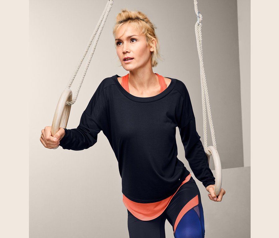 Frau hält Turnringe und trägt ein 2-in-1-Sportshirt.