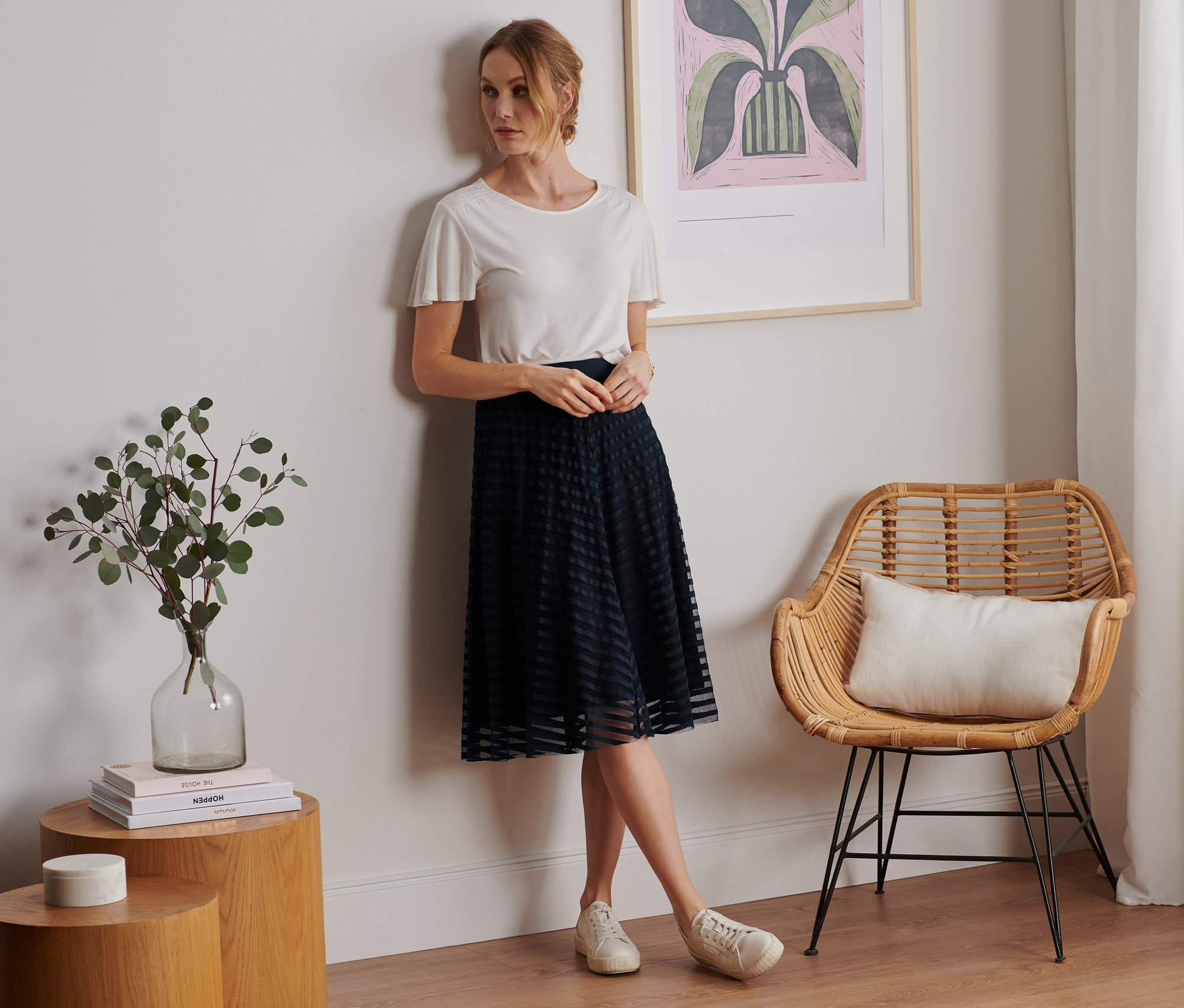Frau lehnt an Wand und trägt ein weißes T-Shirt und einen Meshrock.