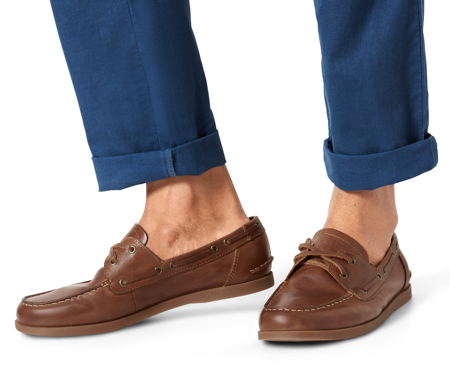 Füße eines Mannes in blauen Hosen und Leder-Bootsschuhen.