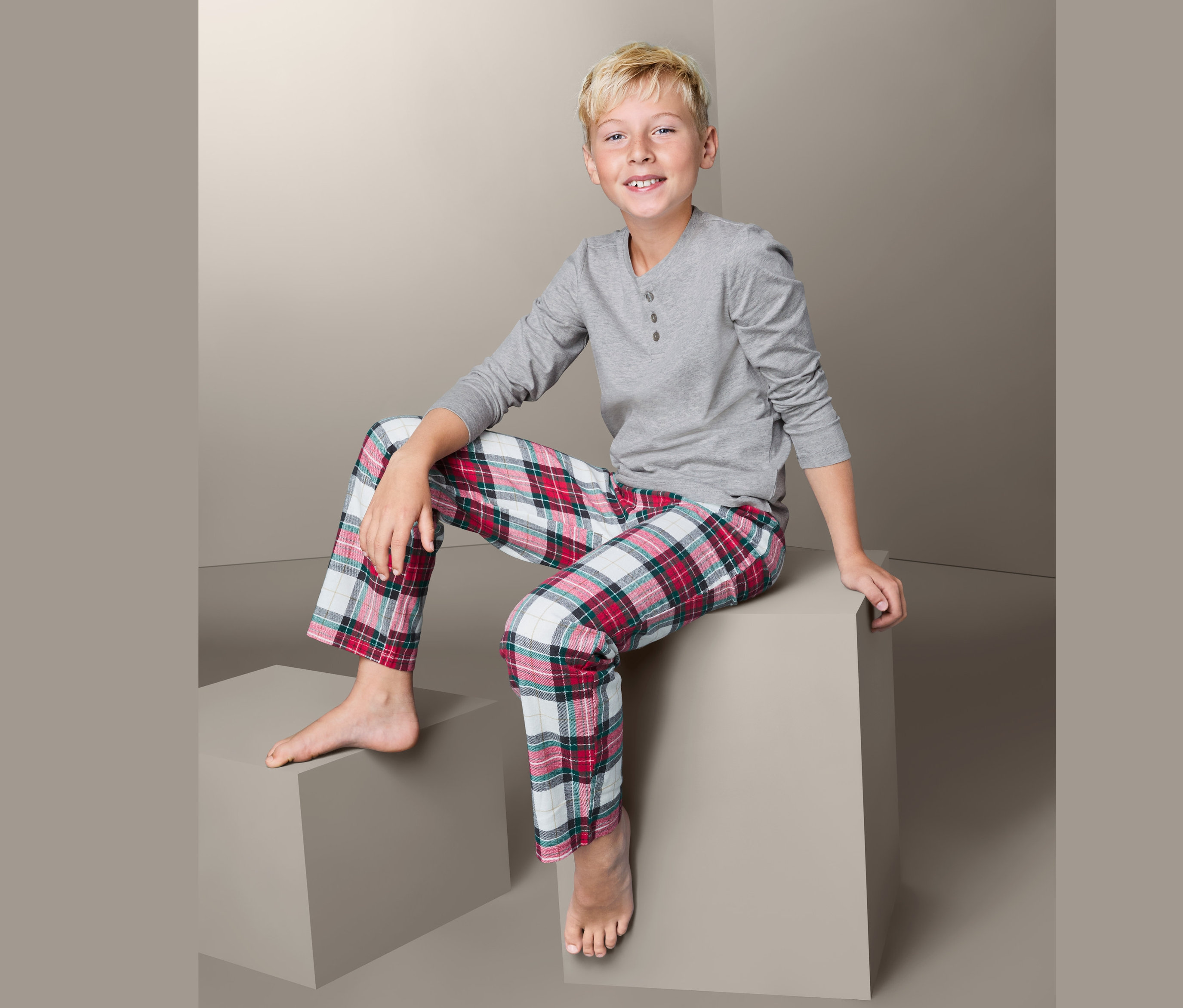 Junge sitzt auf einem grauen Würfel und trägt einen Pyjama.