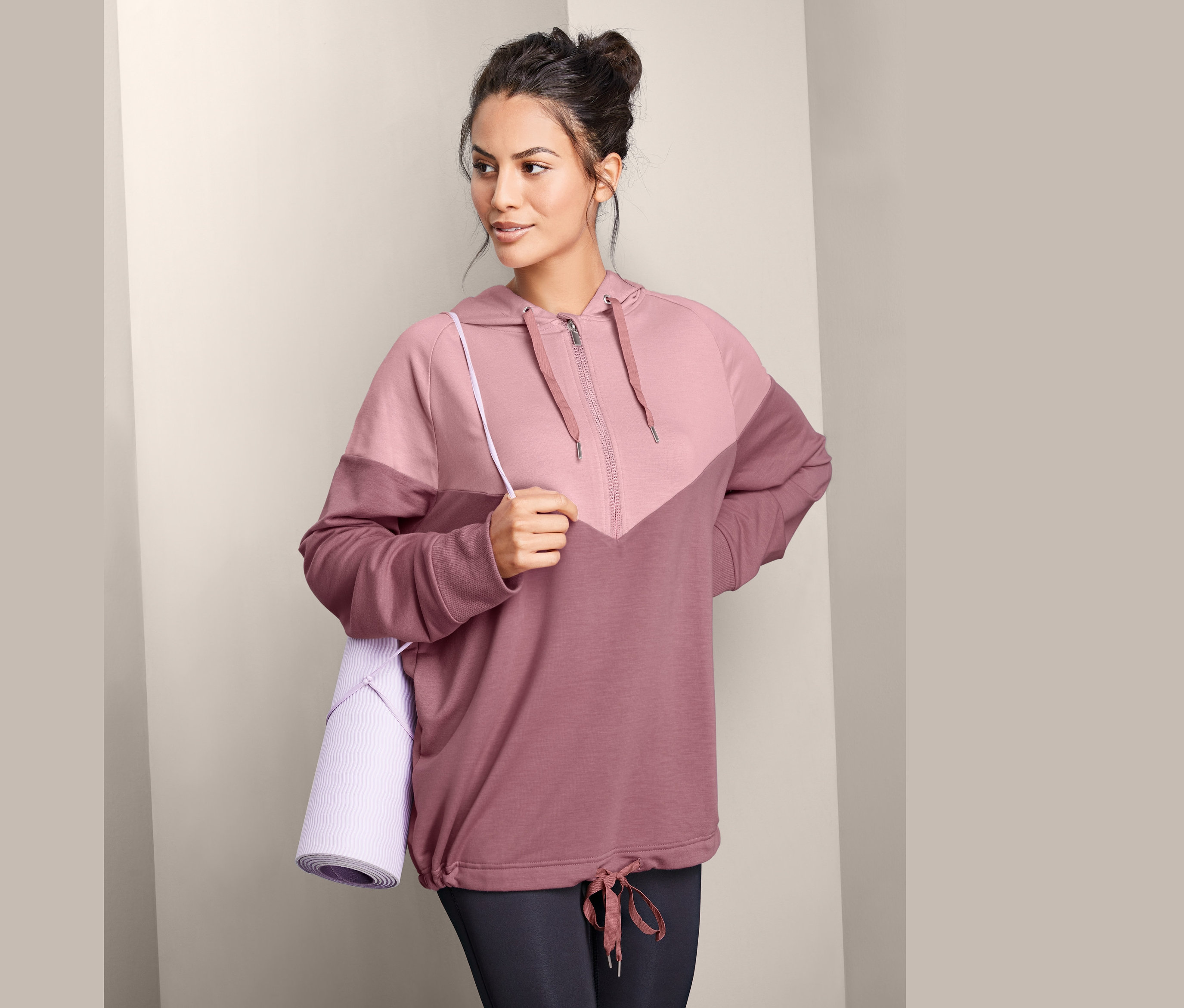 Frau trägt einen Sweatpullover und hält eine Yogamatte.