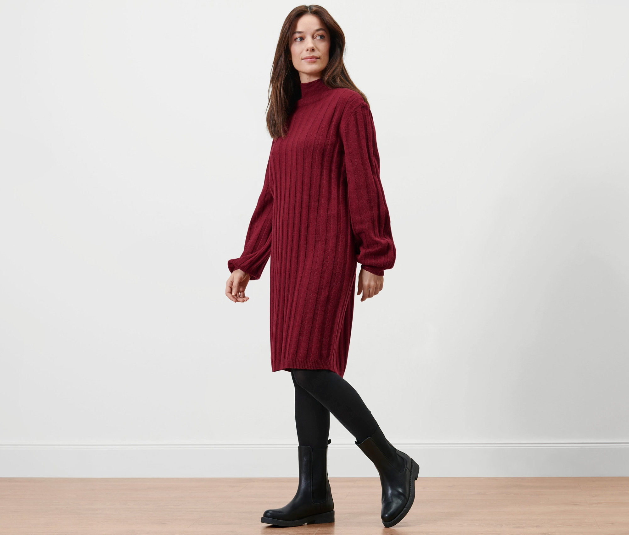 Frau geht, trägt geripptes Strickkleid mit Stehkragen, schwarze Leggings und Stiefel.