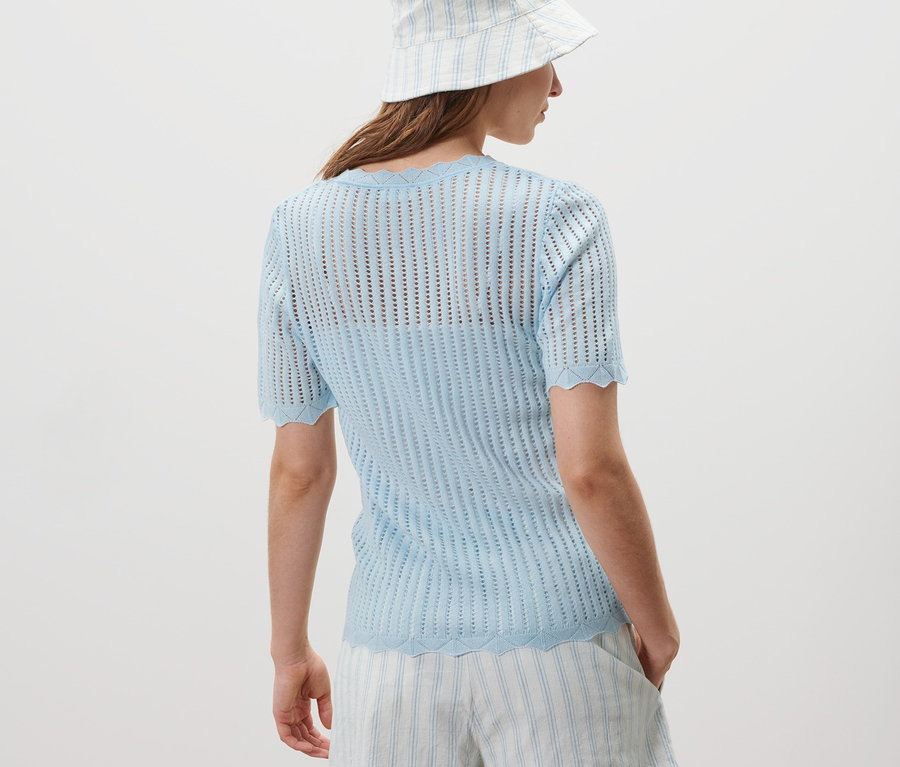 Eine Frau mit dem Rücken zur Kamera trägt ein eisblaues Strick-Shirt und gestreifte Shorts.