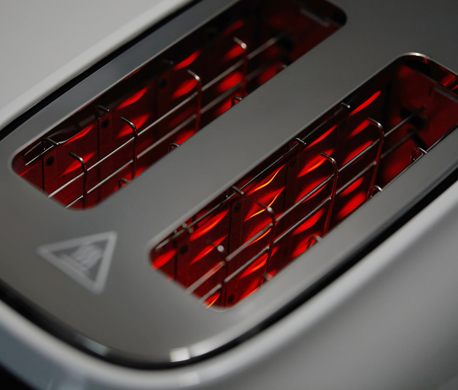 Detailansicht eines weißen Toasters mit rot glühenden Heizspiralen.