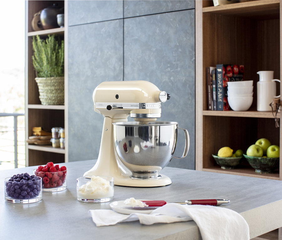 Eine creme-farbene KitchenAid Küchenmaschine »Artisan 5KSM125EAC« steht auf einer grauen Arbeitsplatte neben Gläsern mit Blaubeeren, Himbeeren und Schlagsahne.
