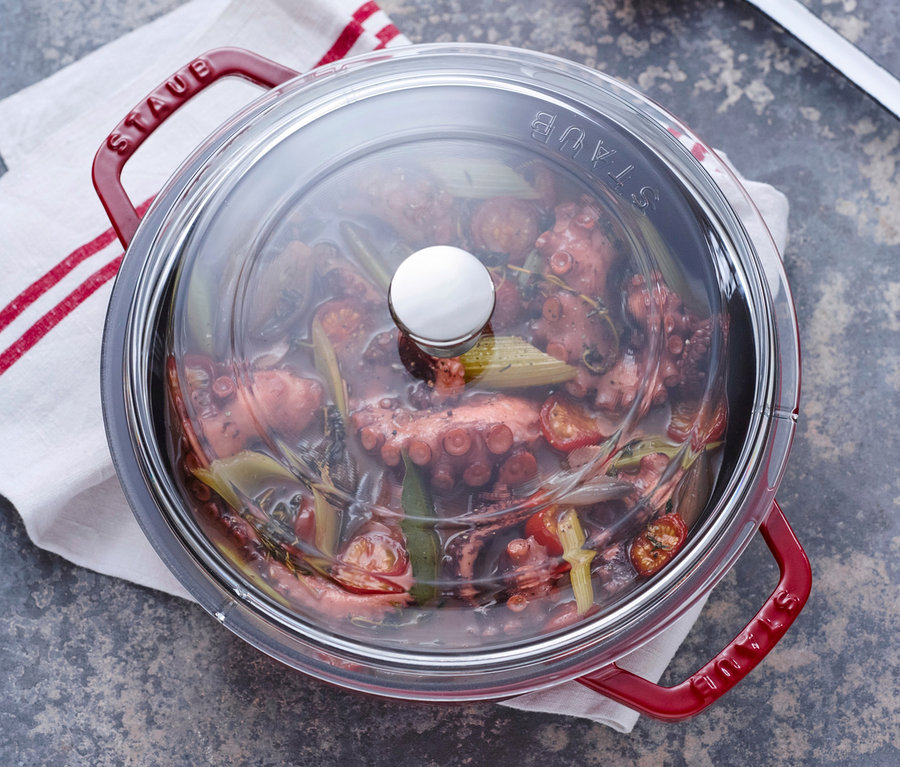 Ein roter STAUB Gusseisen-Bräter »Braisers« mit Glasdeckel und gekochtem Oktopus liegt auf einem Küchentuch.