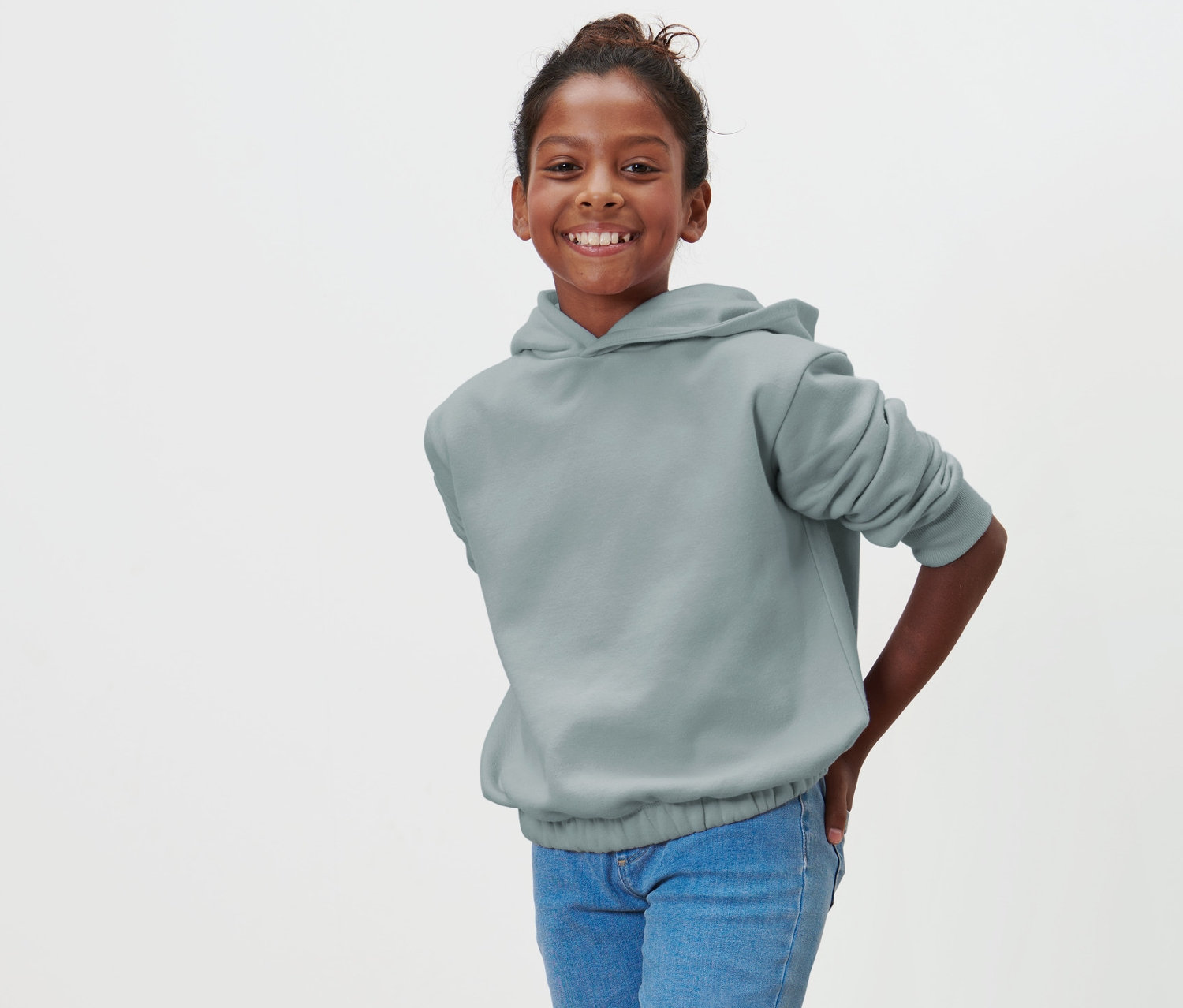 Ein lächelndes Mädchen posiert in einem Kinder-Sweat-Hoodie und blauen Jeans.