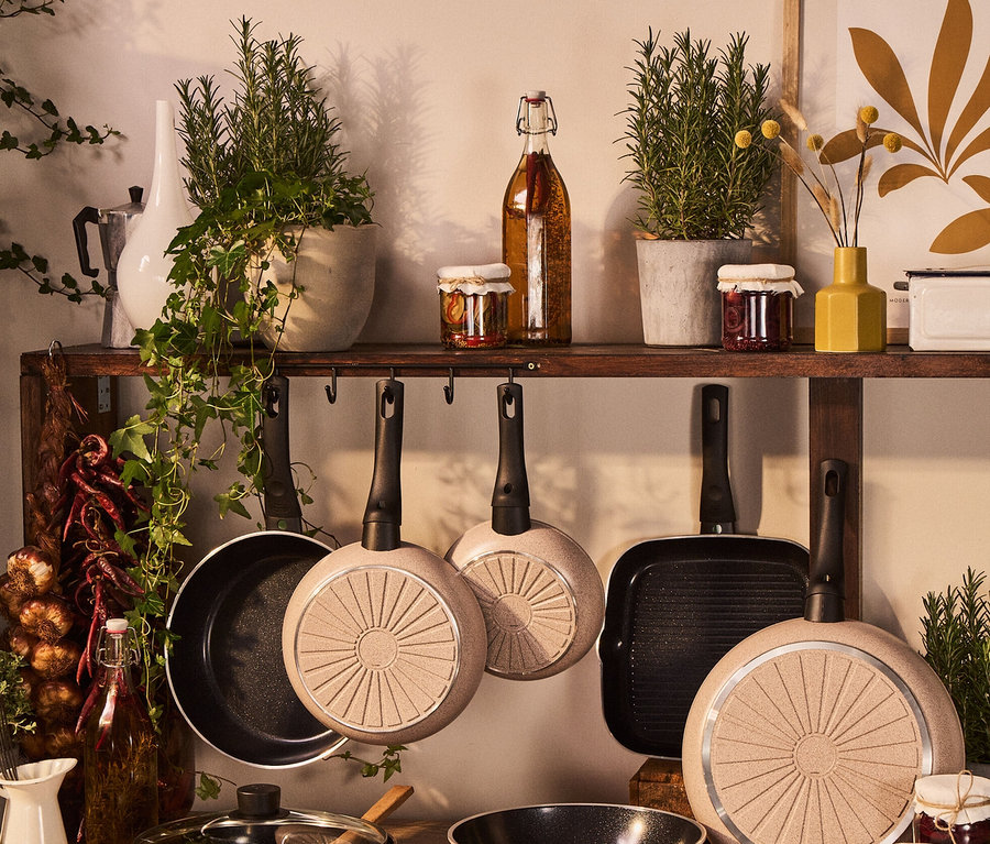 Küchenstillleben mit verschiedenen Töpfen und Pfannen, darunter eine sandfarbene BALLARINI Aluminium-Bratpfanne, 24 cm.
