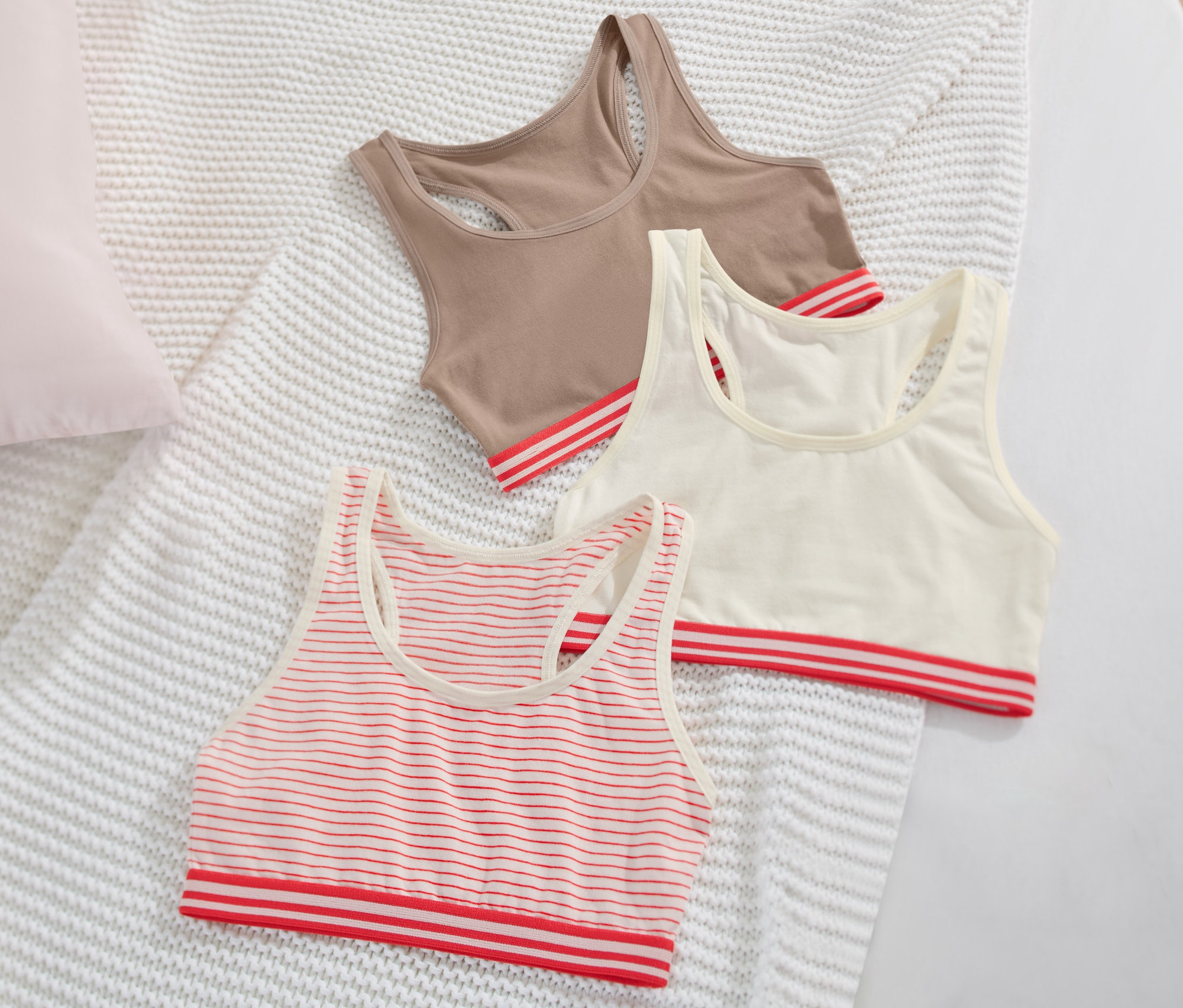 Drei Mädchen-Bustiers liegen auf einer weissen Strickdecke.