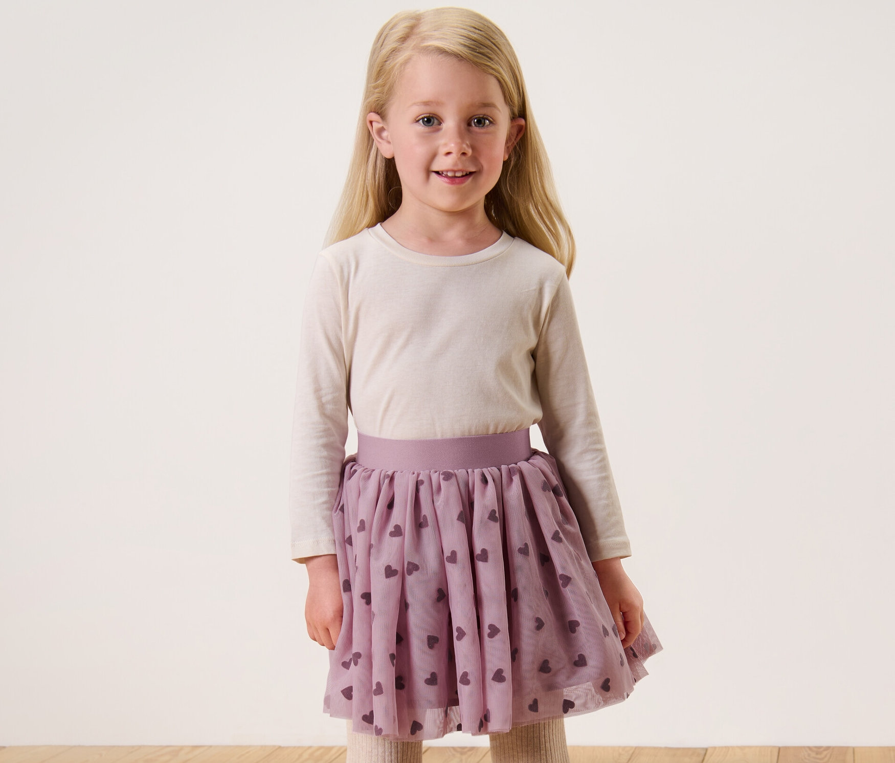 Lächelndes blondes Mädchen im Kinder-Tüllrock mit Herzchenmuster.