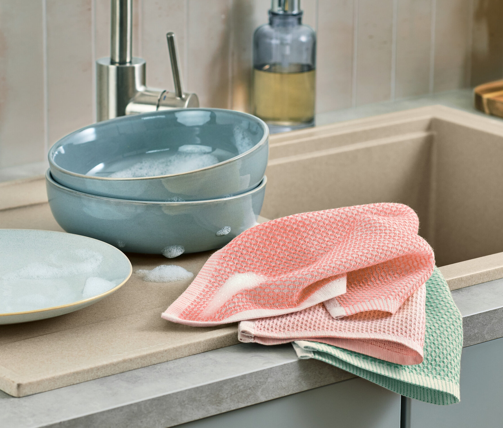 Zwei blaue Schüsseln mit Schaum stehen nebeneinander auf einer Abtropffläche, daneben liegen 3 Spültücher.