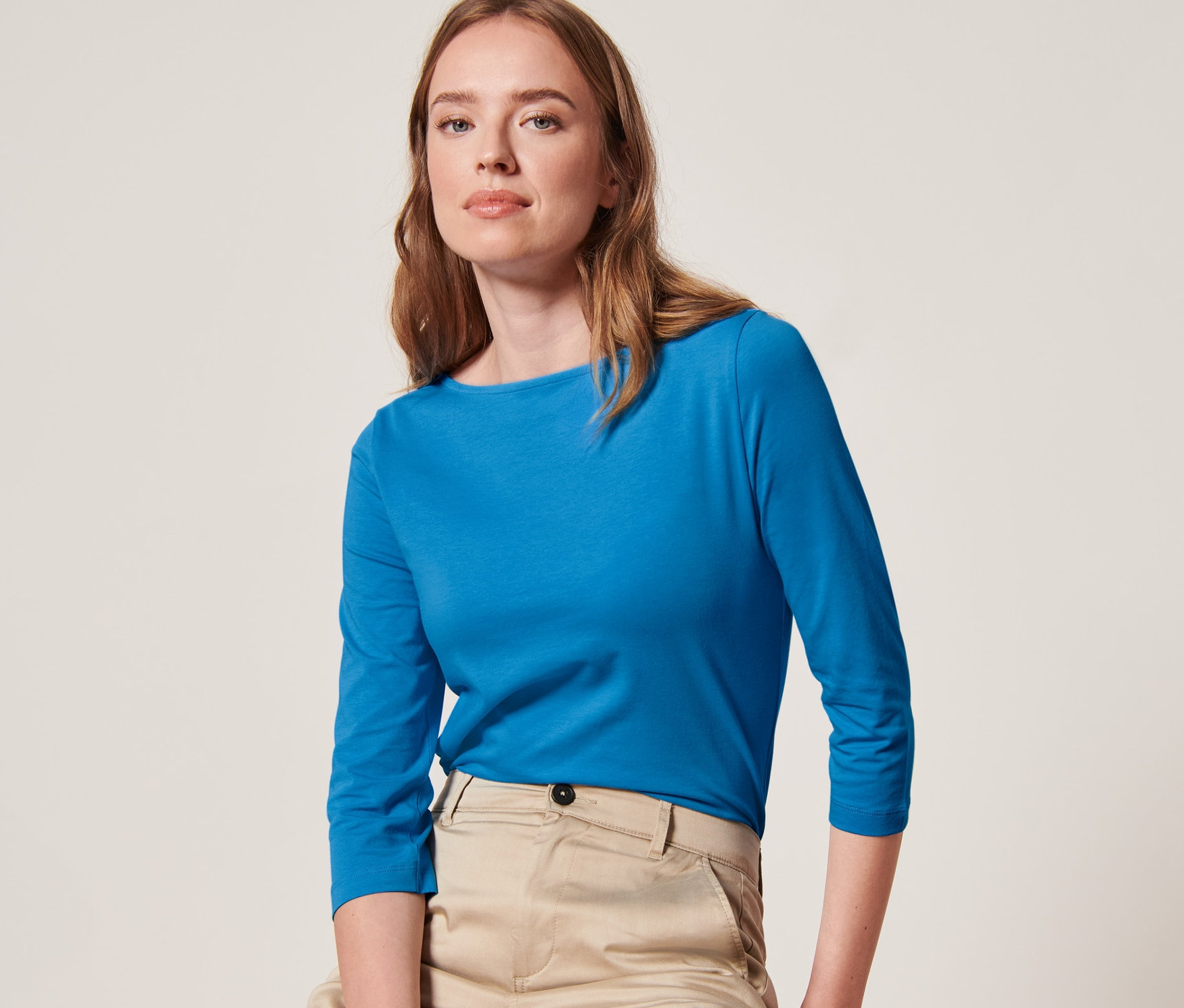 Eine Frau sitzt auf einem Hocker und trägt ein azurblaues Shirt mit 3/4-Arm.