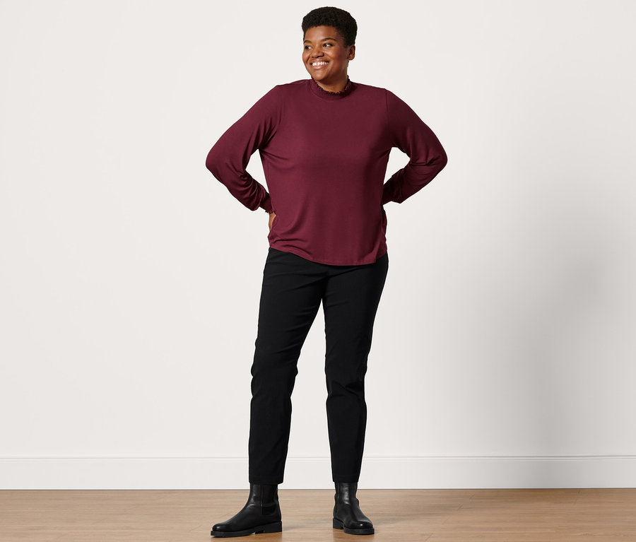 Frau posiert in Lederboots, schwarzer Konfektionierter Bengalinhose und Blusenshirt mit Stehkragen.