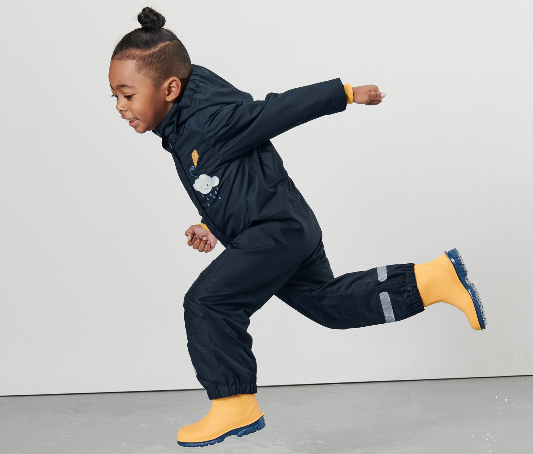 Ein Kind in einem Kleinkind Regen-Einteiler springt in eine Pfütze.