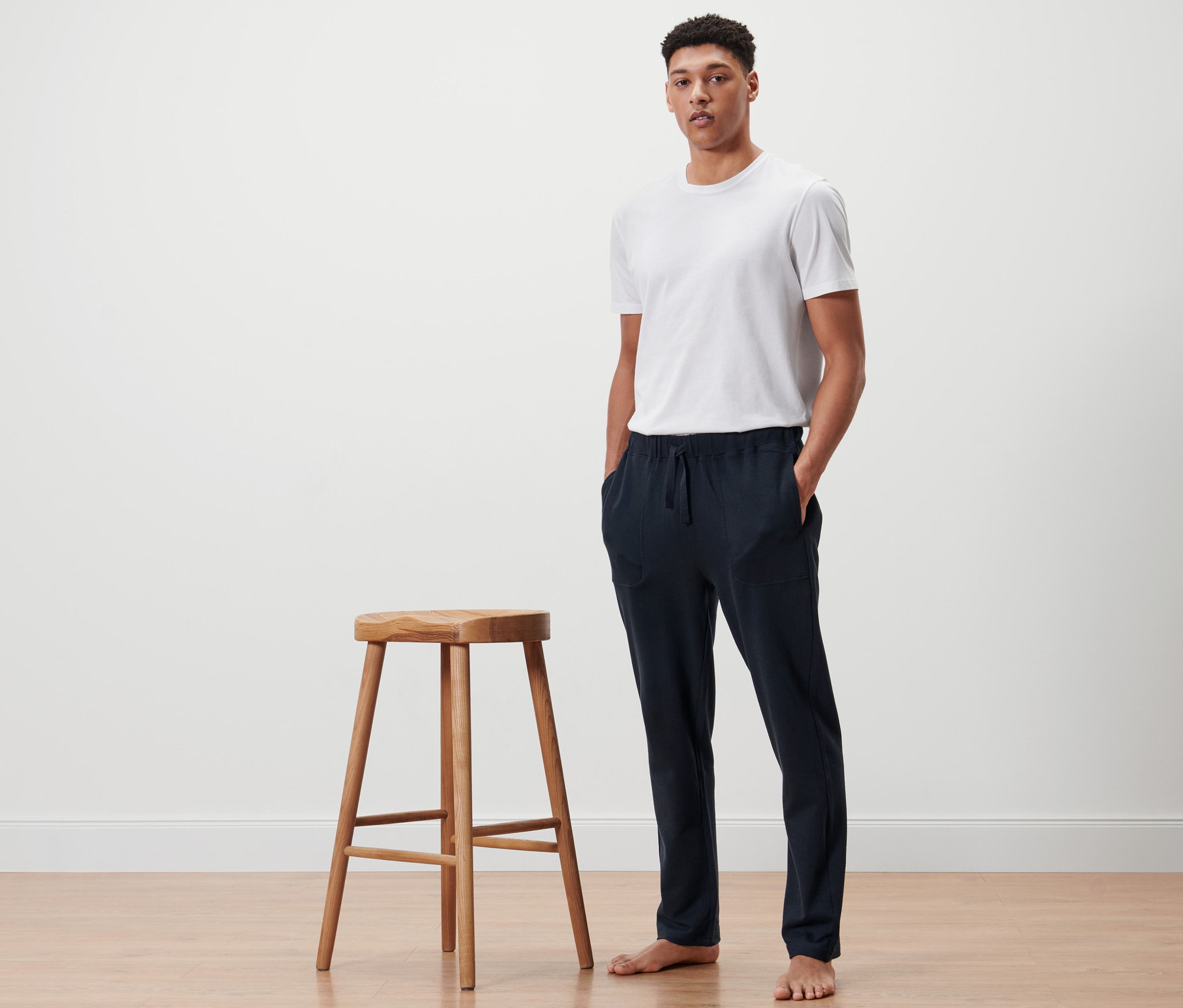 Mann steht neben einem Holzhocker und trägt eine dunkelblaue Homewearhose.