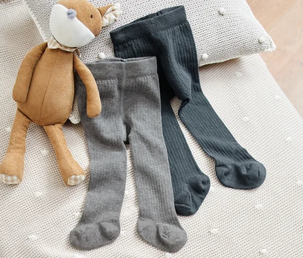 Zwei Paar Baby-Strumpfhosen liegen neben einem Plüschtier auf einer Strickdecke.