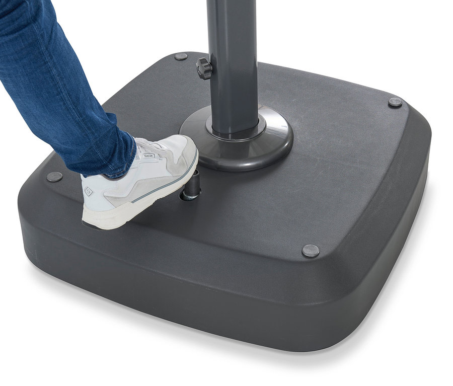 Ein Bein in Jeans und einem weißen Schuh steht auf dem grauen Sockel eines Sonnenschirms.