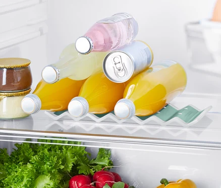 Im Kühlschrank befindet sich ein Kühlschrank-Flaschenhalter, auf dem drei Saftflaschen und eine Dose liegen. Im unteren Bereich sind Salate, Radieschen und eine gelbe Paprika zu sehen.