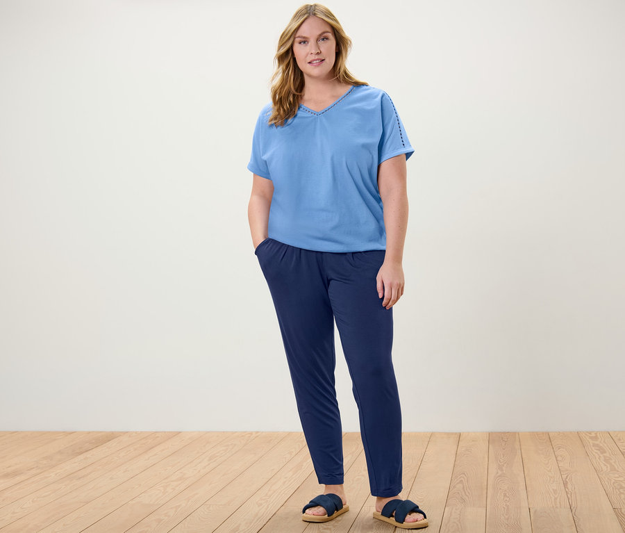 Eine Frau steht und trägt ein hellblaues Blusenshirt mit Crochet-Tape und eine dunkelblaue Jerseyhose.