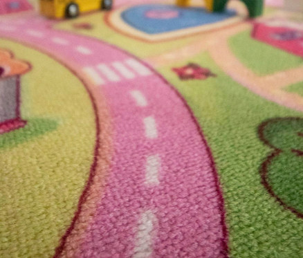 Detailaufnahme eines Kinderspielteppichs »Sweet City« mit Spielzeug darauf.