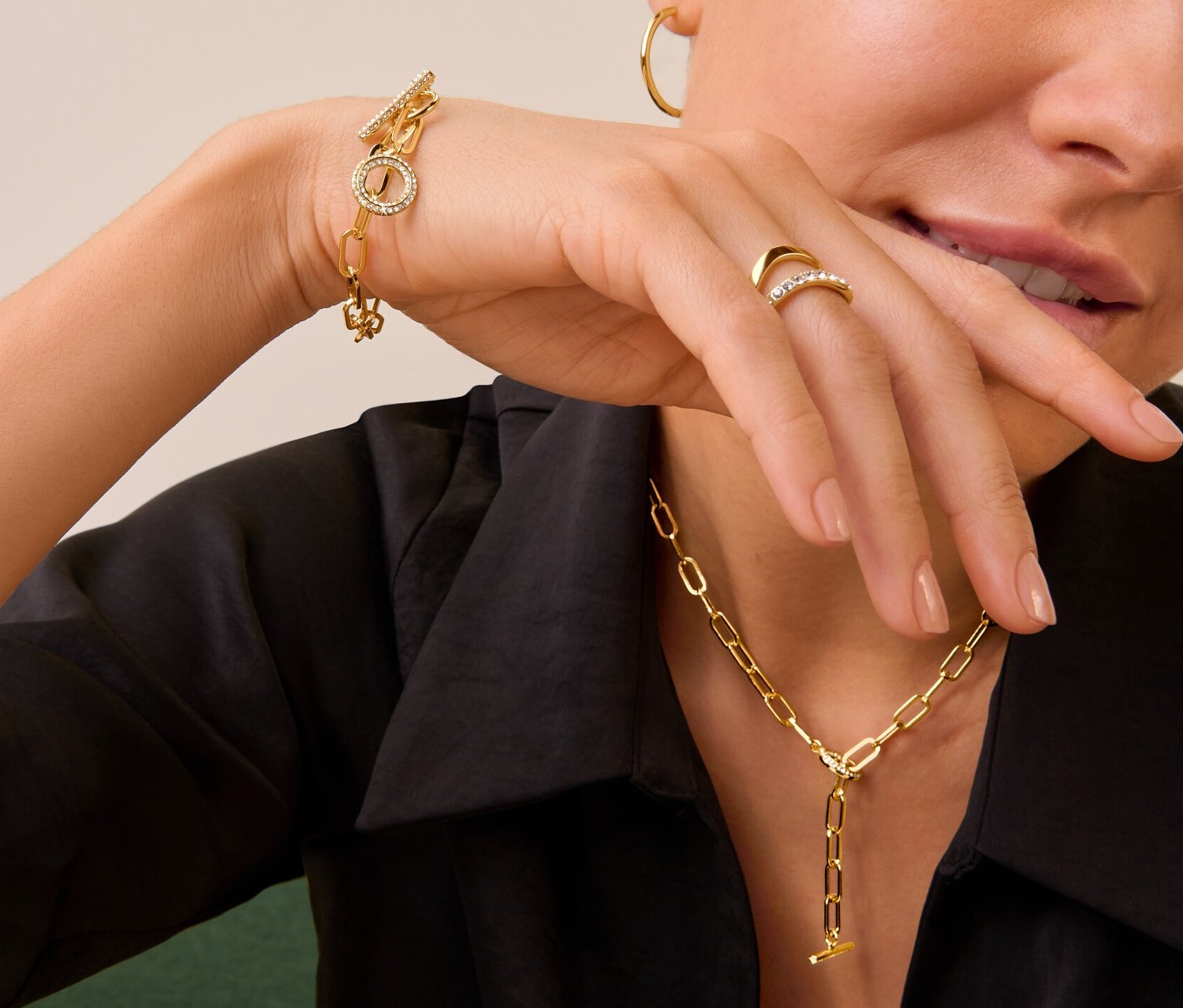 Frau trägt goldenen Ring Doppel-Welle mit Kristallen, Kette und Armband Toggle mit Kristallbesatz und goldfarbene Creolen.