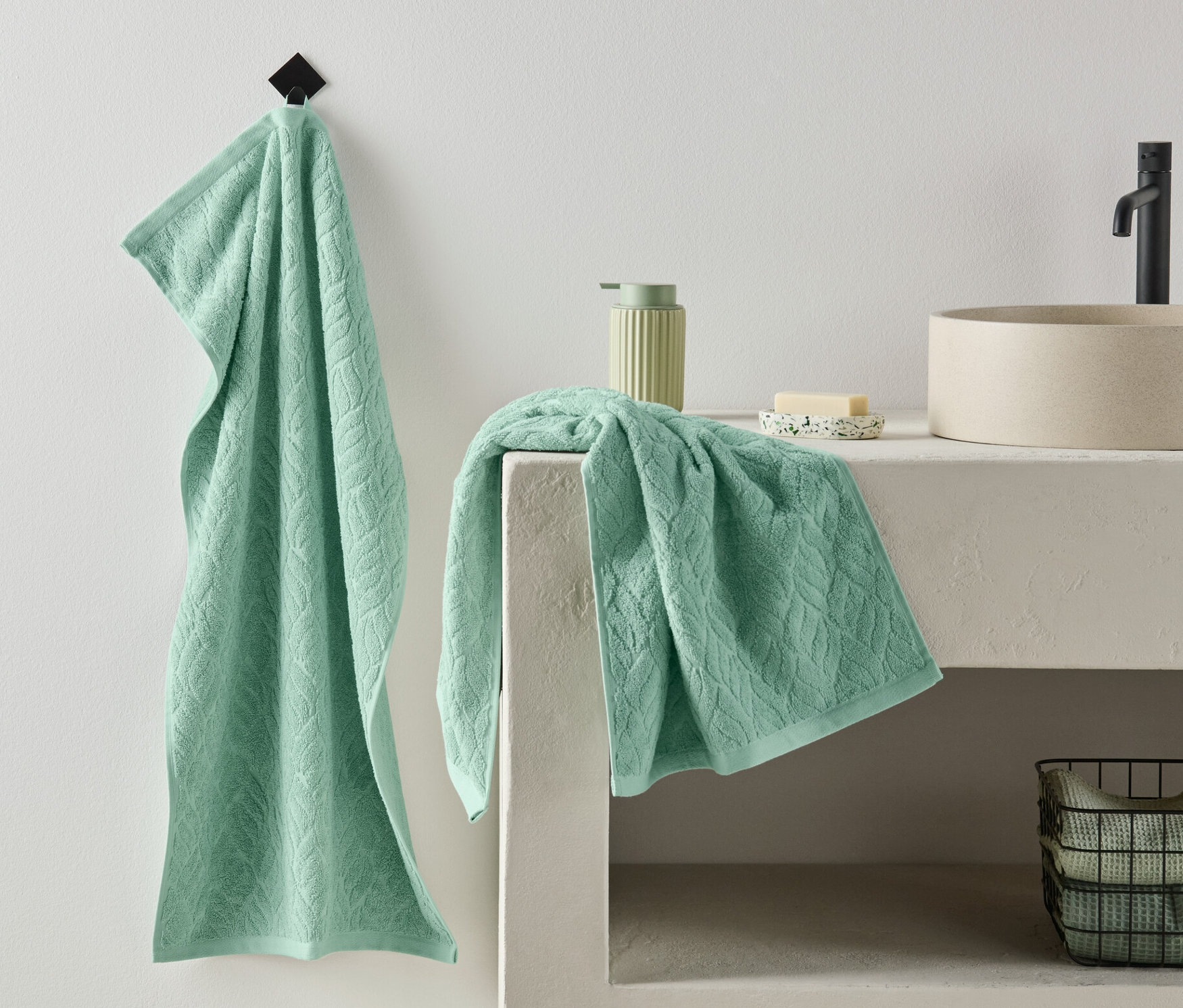 Ein Premium-Handtuch aus einem 2er-Set hängt an der Wand, ein weiteres liegt gefaltet neben einem Waschbecken.