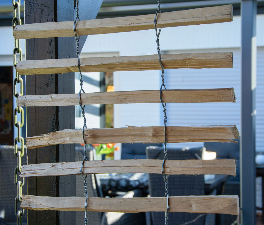 Ein Dobar Rankgitter-Spalier aus Holz, das an Ketten hängt. Im Hintergrund sind Gartenmöbel zu sehen.