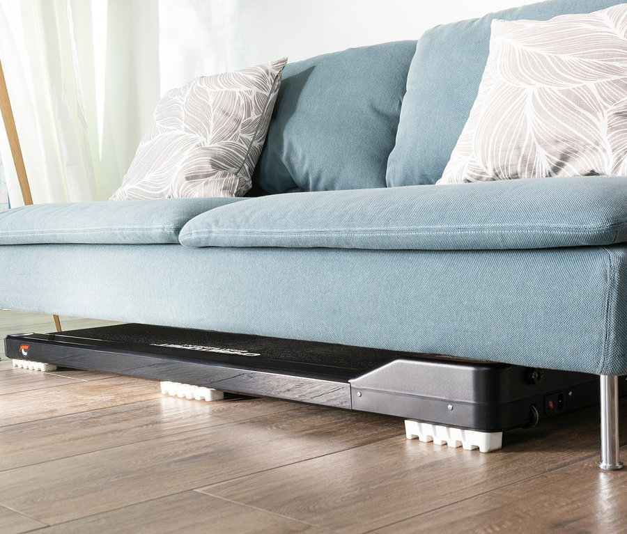 Ein schwarzes Christopeit Sport Walking Pad 4.0 steht unter einem blauen Sofa.