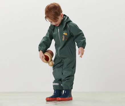 Junge spielt im Kinder-Softshell-Einteiler mit einem Wasserspielzeug.