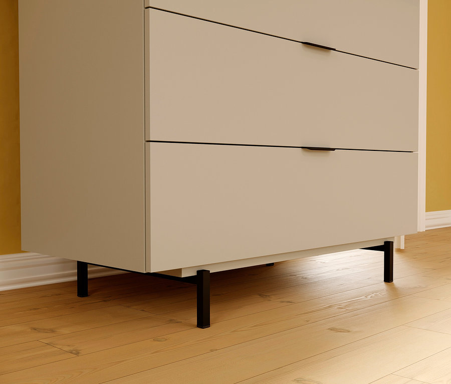 Detailaufnahme einer beigen Wickelkommode »Tomino« mit drei Schubladen und schwarzen Füßen auf einem Holzboden.