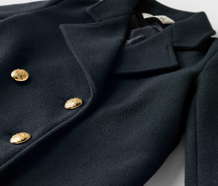 Detailaufnahme eines dunkelblauen zweireihigen Mantels mit goldenen Knöpfen.