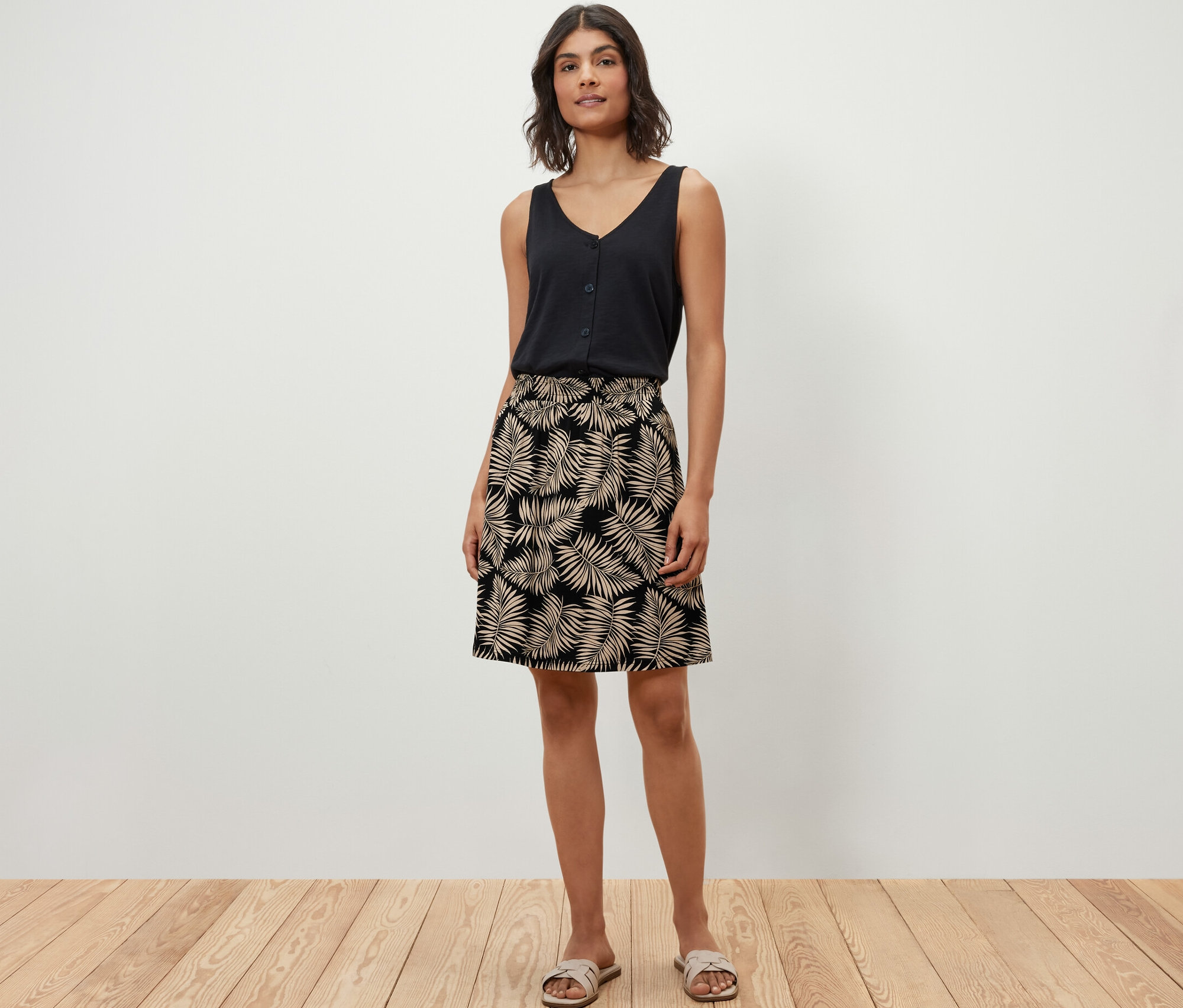 Frau posiert in schwarzem Top und bedrucktem Jerseyrock auf Holzboden.