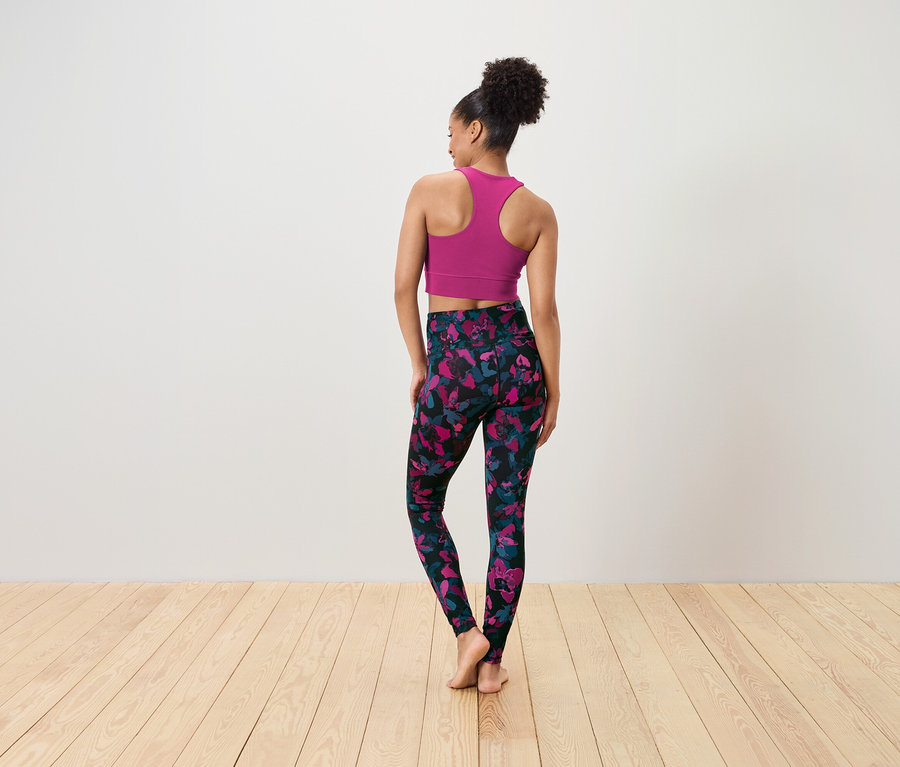 Frau mit dem Rücken zur Kamera trägt einen pinkfarbenen Sport-BH und schwarze Leggings mit rosa-blauem Blumenmuster.