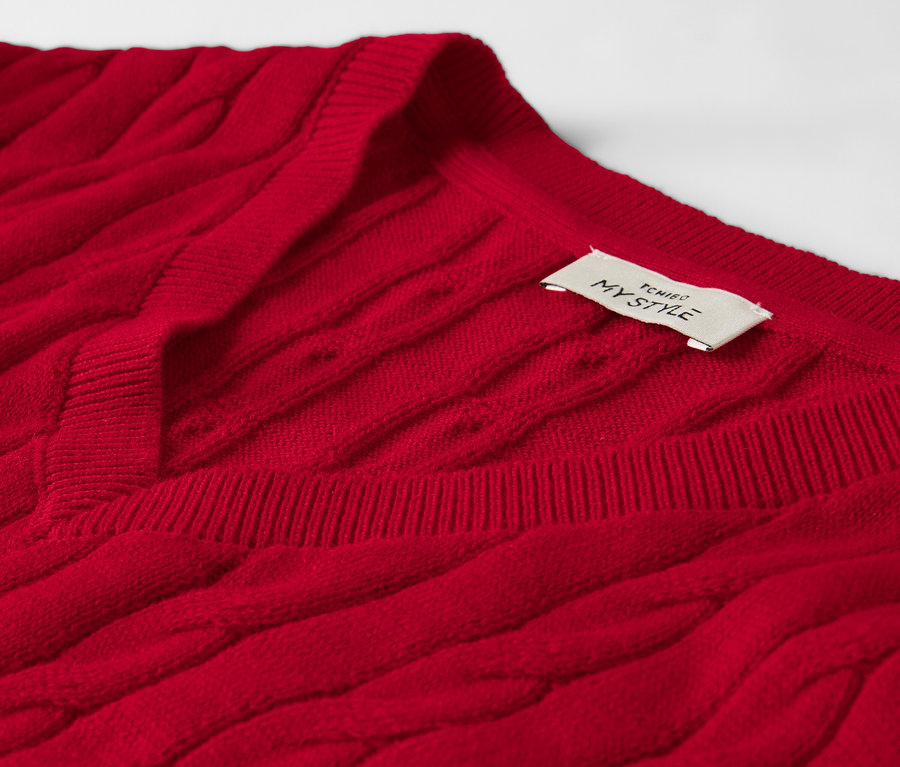 Detailansicht eines roten Zopfstrickpullovers mit einem Etikett am Halsausschnitt.