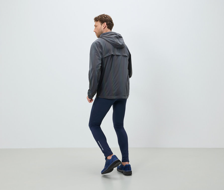 Ein Mann in einer grauen Kapuzenjacke, dunkelblauen Leggings und Turnschuhen steht mit dem Rücken zum Betrachter.