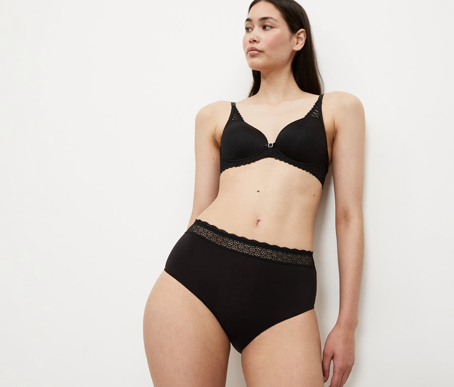 Eine Frau trägt einen schwarzen BH und schwarze Triumph Feel of Modal Midi Slips mit Spitzenbesatz.