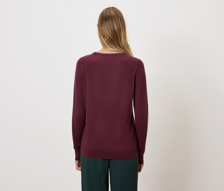 Rückansicht einer Frau mit blonden Haaren, die einen burgunderroten Pullover und eine grüne Hose trägt.