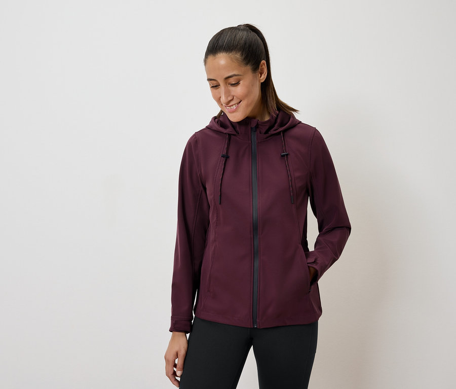 Frau trägt eine burgunderfarbene Kapuzenjacke und schwarze Leggings.