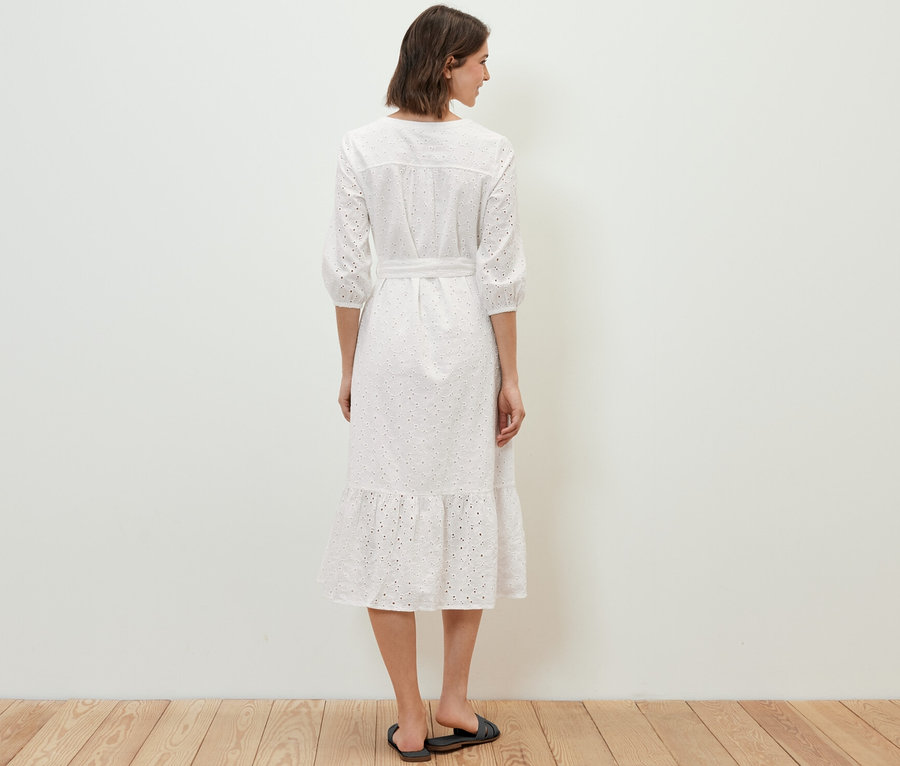 Frau steht mit dem Rücken zur Kamera und trägt ein Blusenkleid mit Lochstickerei.