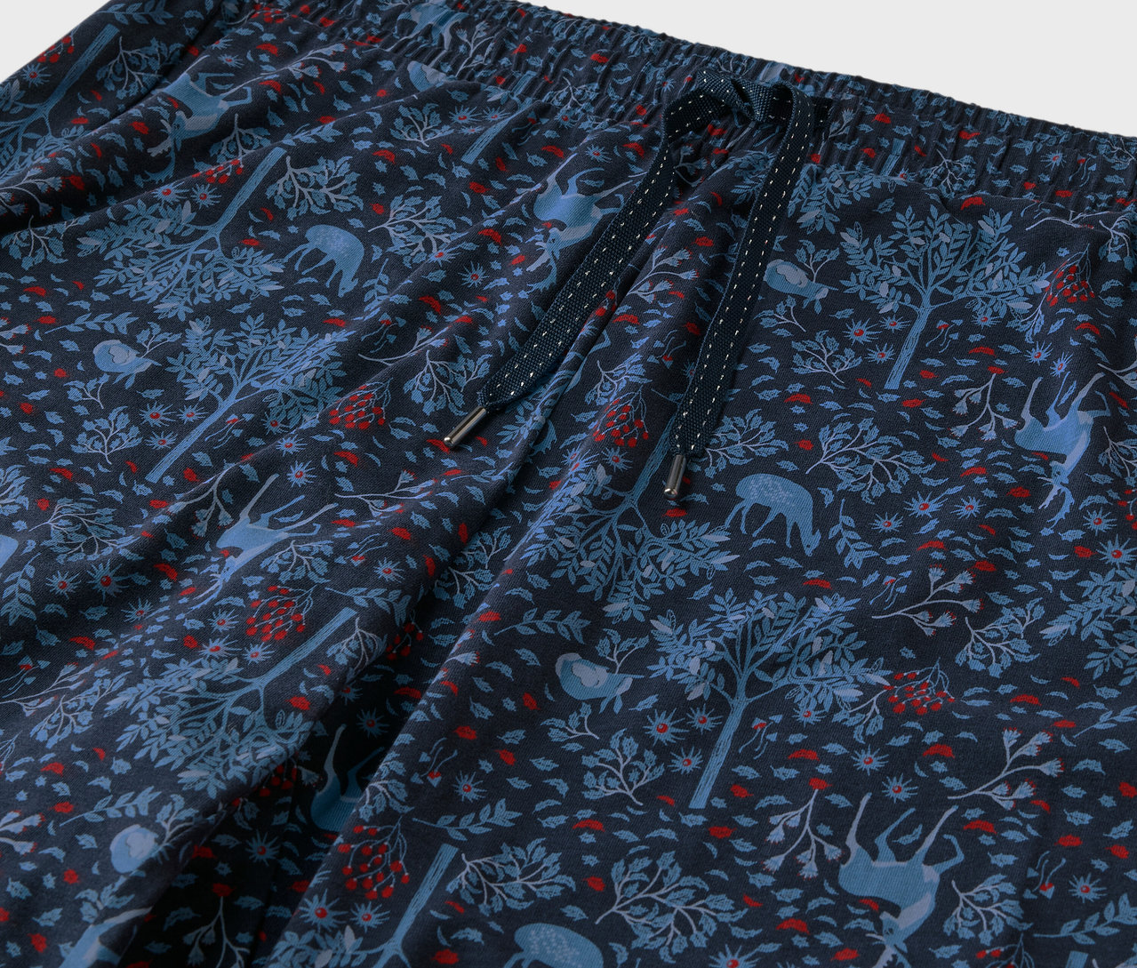 Detailaufnahme einer blauen Hose mit einem Muster aus Wald, Bäumen und Hirschen.