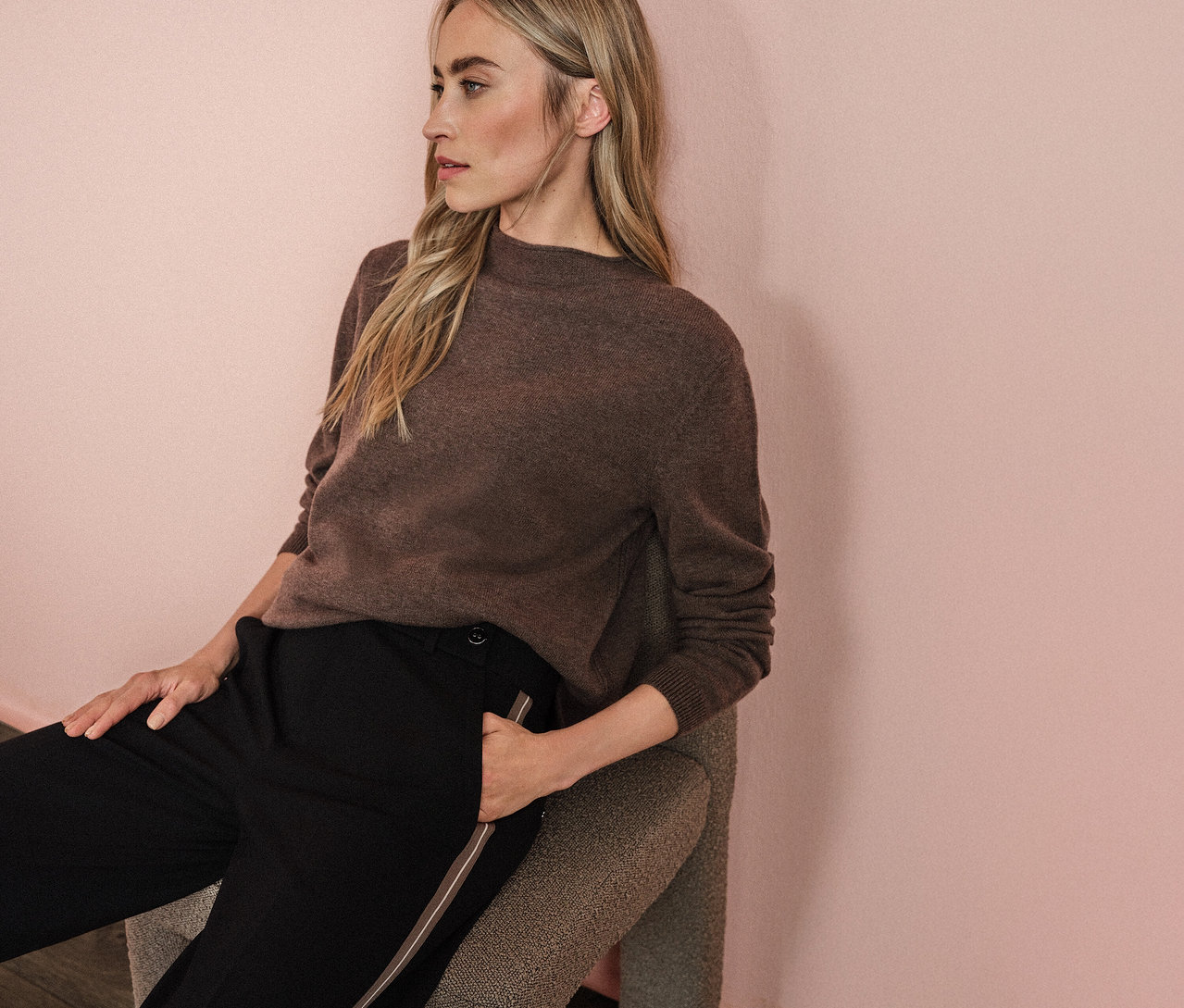 Frau sitzt auf einem Stuhl und trägt einen braunen Pullover und eine schwarze Street One Straight Leg Hose mit Gallon.