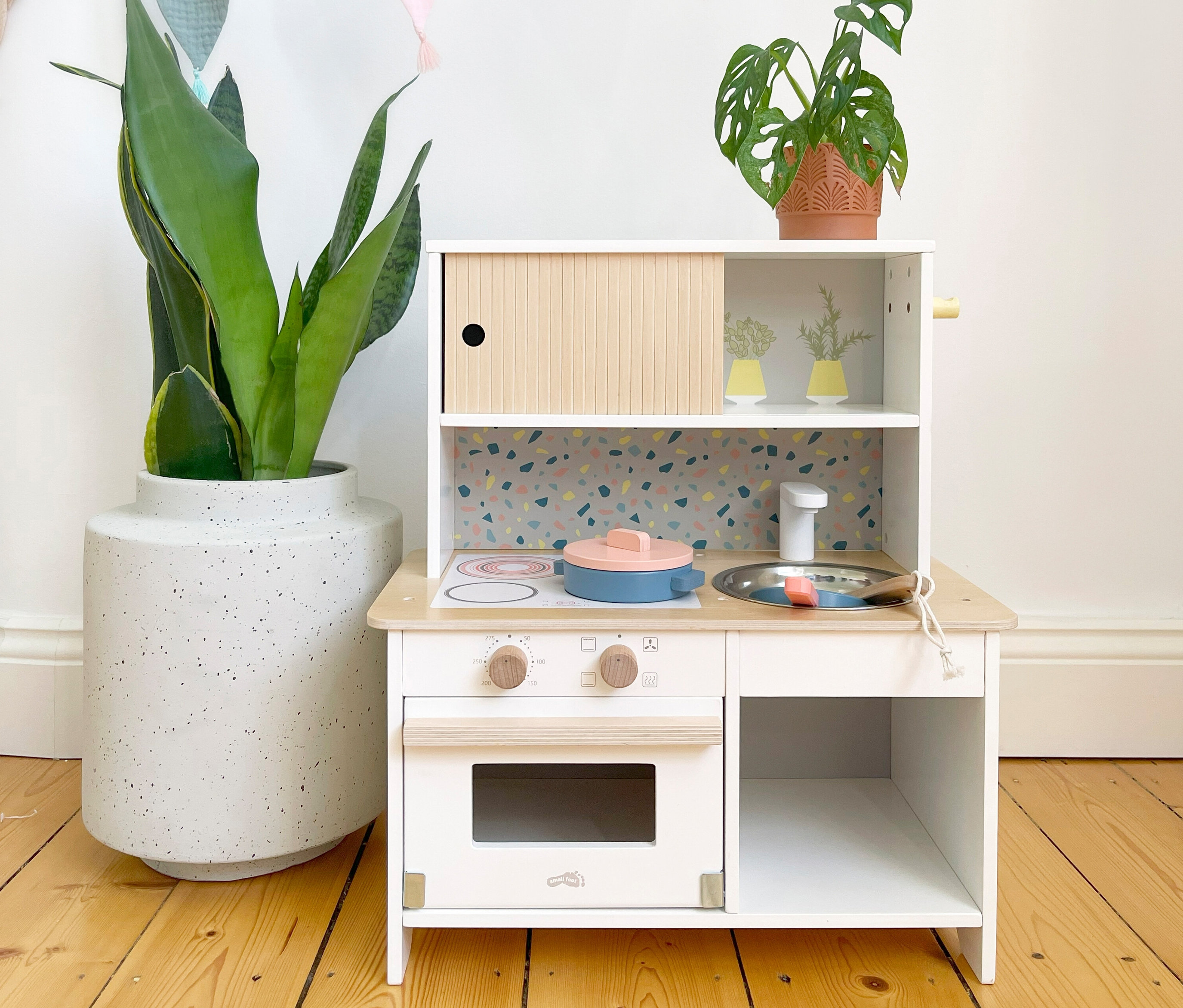 Eine kleine, weiße small foot Kinderküche »Terrazzo« steht auf einem Holzboden.