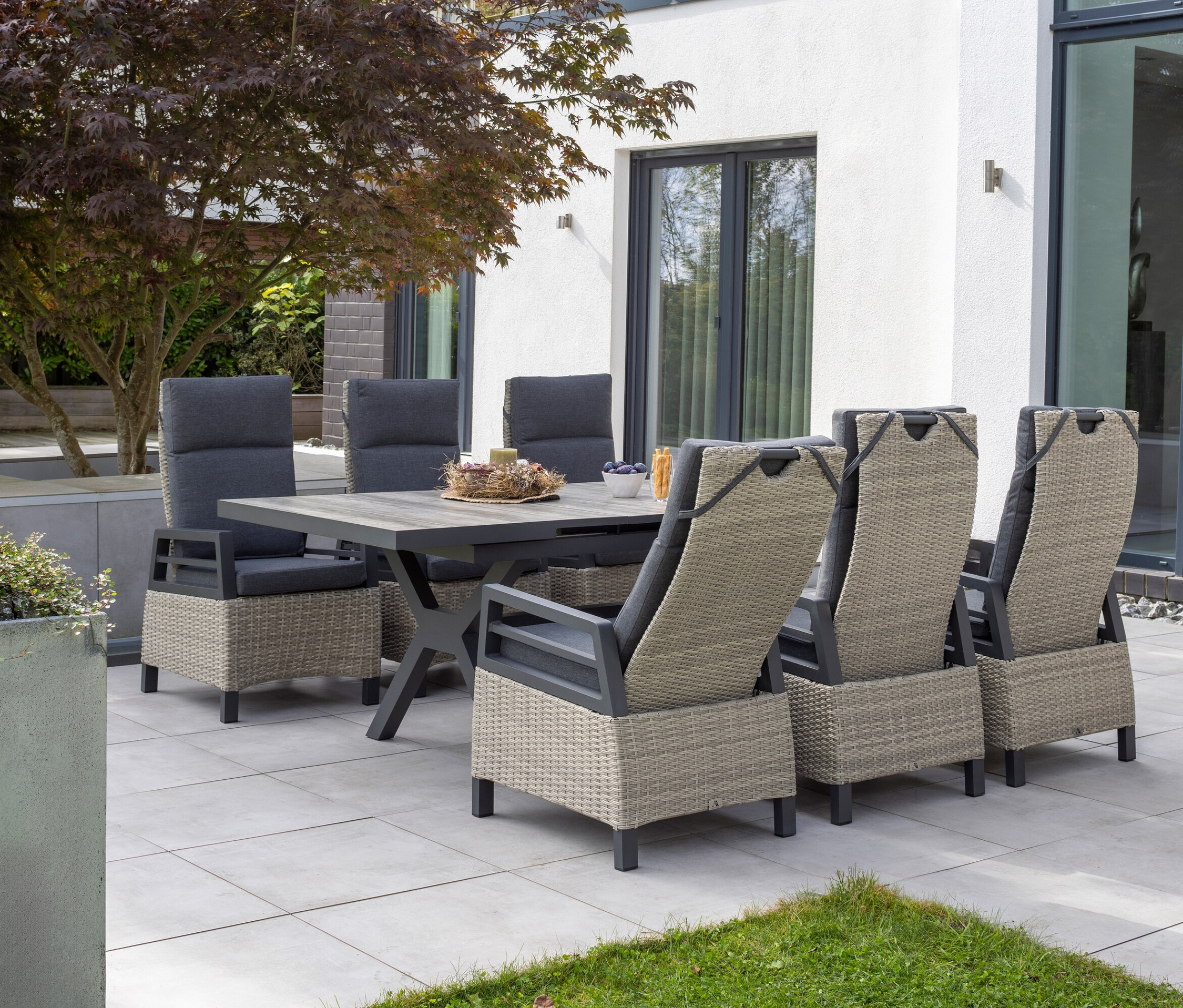 Ein Essbereich im Freien mit sechs Stühlen und einem rechteckigen Tisch steht auf einer Terrasse.