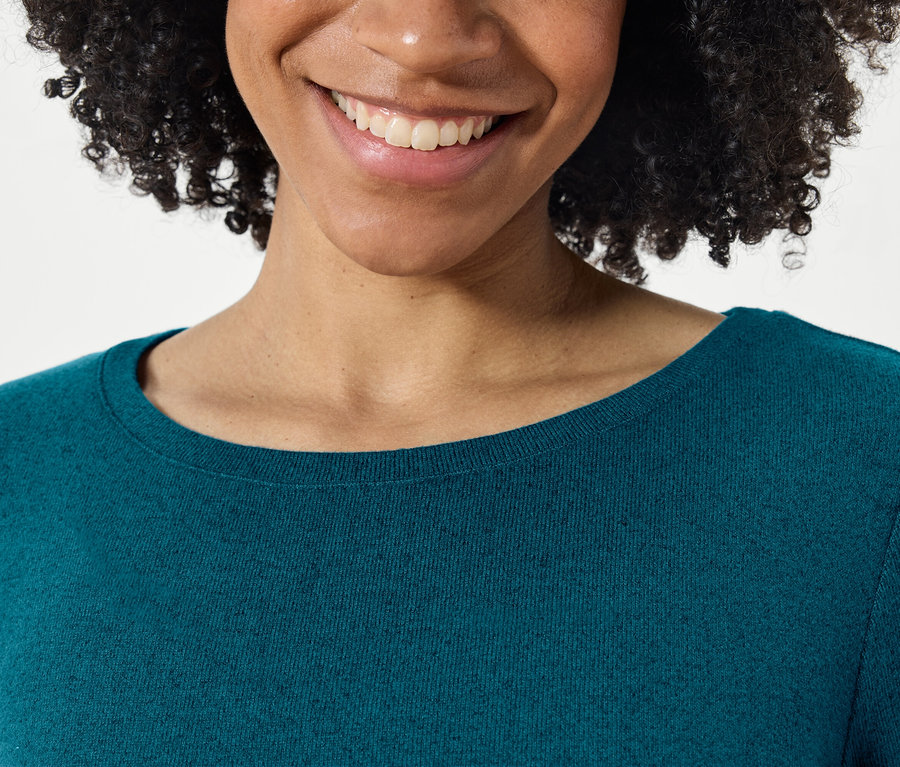 Detailaufnahme einer lächelnden Frau mit Afrofrisur in einem blaugrünen Pullover.