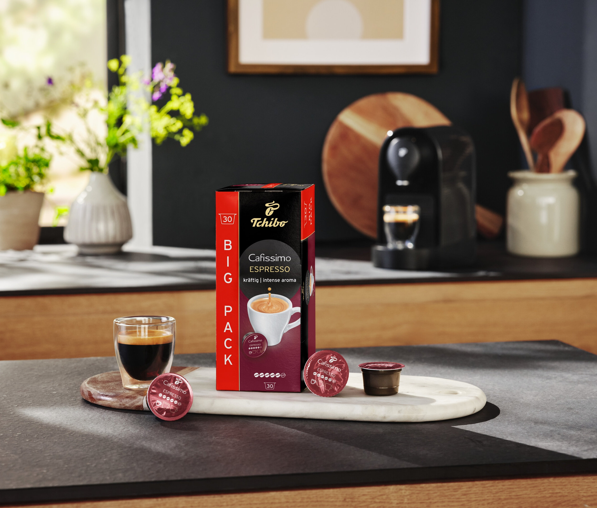 Espressoglas steht neben Packung Cafissimo Espresso kräftig und Kapseln auf Marmortablett.